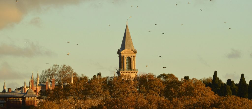 Topkapi Palace Architecture has The iconic Tower of Justice (Adalet Kulesi), a symbol of Ottoman imperial architecture, rising majestically above the golden autumn trees at sunset.